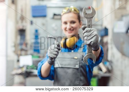 Woman mechanic showing tools to the camera holding wrench in her hand