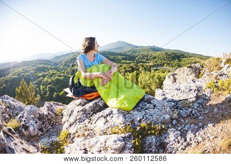 A Woman Is Sitting In A Sleeping Bag At Sunset. Camping On Top Of A Mountain. A Smiling Girl Rests A