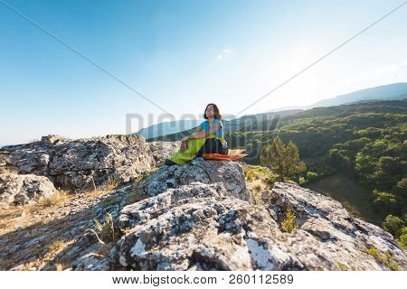 A Woman Is Sitting In A Sleeping Bag At Sunset. Camping On Top Of A Mountain. A Smiling Girl Rests A