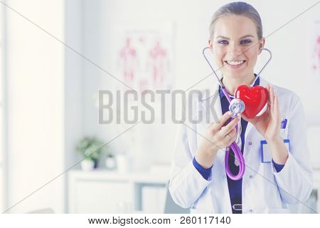 A doctor with stethoscope examining red heart, isolated on white background