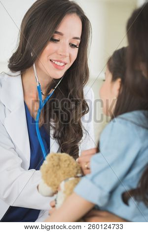 Female doctor and little girl with teddy bear sitting at the medical office.Child and doctor examining teddy bear