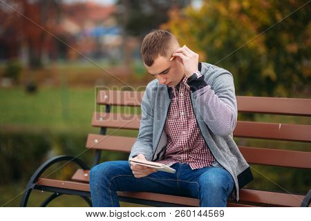 A Cute Student Sits On The Bench And Writes Down His Thoughts In His Notebool Using A Pensil. Study 