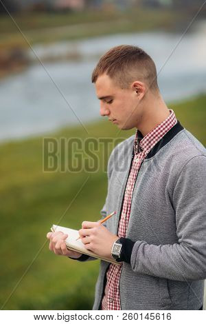 A Cute Student Writes Down His Thoughts In His Notebool Using A Pensil