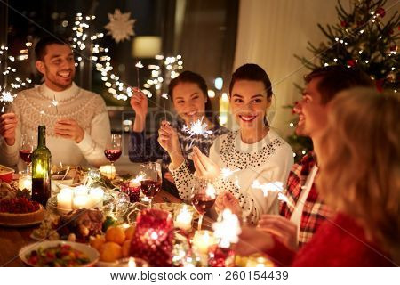 winter holidays and people concept - happy friends with sparklers celebrating christmas at home feast
