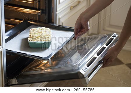 Woman Cooking In The Kitchen, Puts Cake In The Oven. Putting A Cake Into An Oven At The Home Kitchen