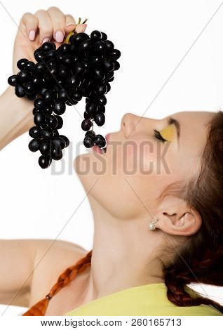 Beautiful Redhead Woman Is Eating Black Grapes. Concept Of Healthy Eating
