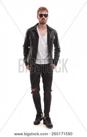 sexy blond man wearing black sunglasses and leather jacket standing on white background, full length picture
