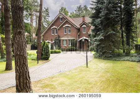 Large, Rural Estate With Brick Facade And Green Lawn Standing In The Forest Among Trees