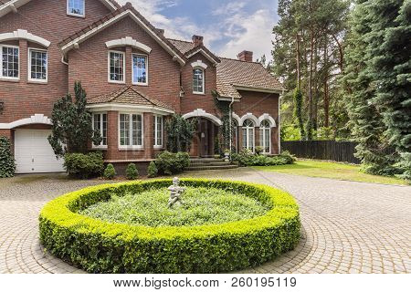 Round Hedge And A Small Statue In The Middle Of A Cobblestone Driveway To An Elegant, English Style