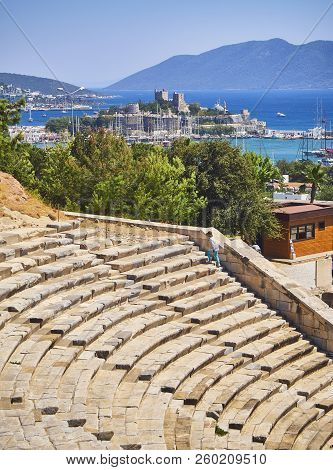Bodrum, Turkey - July 6, 2018. An Asian tourist  visiting the Amphitheatre of Halicarnassus with Kumbahce bay and the Castle of Saint Peter in the background. Bodrum, Mugla Province, Turkey.