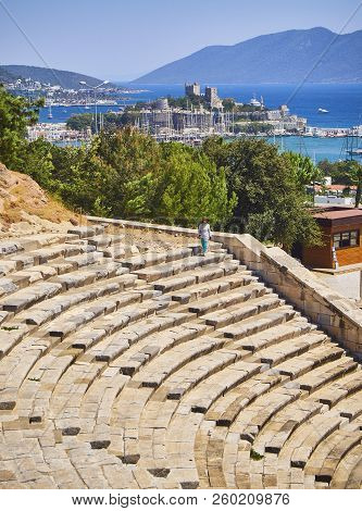 Bodrum, Turkey - July 6, 2018. An Asian tourist  visiting the Amphitheatre of Halicarnassus with Kumbahce bay and the Castle of Saint Peter in the background. Bodrum, Mugla Province, Turkey.