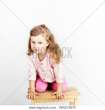 Cute Little Child Sitting On The Chair And Smiling. Wearing Pink Clothes. Portrait Of Adorable Baby