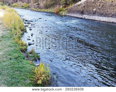 The Beautiful Crooked River With Fall Colored Bushes On Its Banks Flows Through A Canyon Formed From