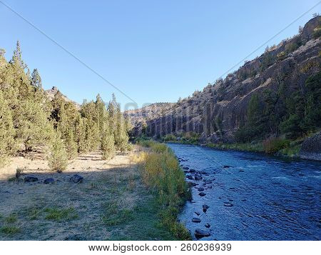 The Beautiful Crooked River With Fall Colored Bushes On Its Banks Flows Through A Canyon Formed From