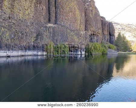 The Beautiful Crooked River With Fall Colored Bushes On Its Banks Flows Through A Canyon Formed From