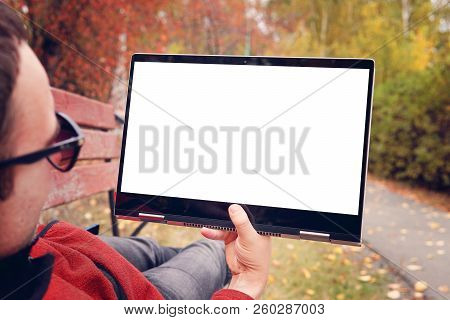 Man Lies On A Bench In The Autumn Park And Looks At The Screen Of A Modern Ultrabook Transformer. Bl