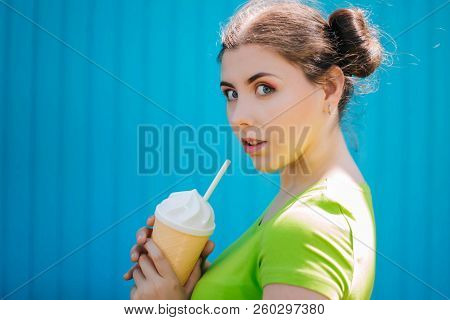 Portrait Of A Girl Against A Bright Blue Wall. Emotional Girl Holding A Plastic Glass With A Refresh