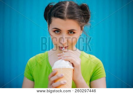 Portrait Of A Girl Against A Bright Blue Wall. Emotional Girl Holding A Plastic Glass With A Refresh