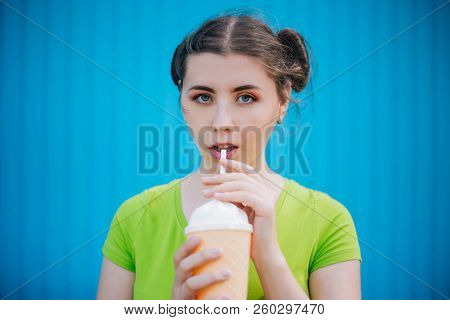Portrait Of A Girl Against A Bright Blue Wall. Emotional Girl Holding A Plastic Glass With A Refresh