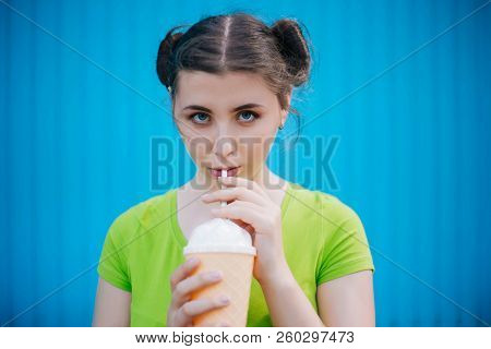 Portrait Of A Girl Against A Bright Blue Wall. Emotional Girl Holding A Plastic Glass With A Refresh