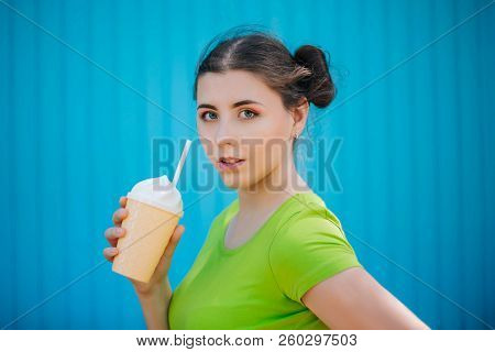 Portrait Of A Girl Against A Bright Blue Wall. Emotional Girl Holding A Plastic Glass With A Refresh