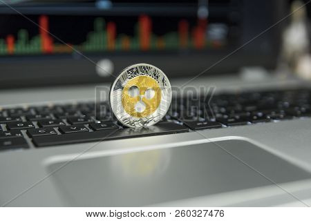 Golden And Silver Ripple Coin On A Black Keyboard Of Silver Laptop And Diagram Chart Graph On A Scre