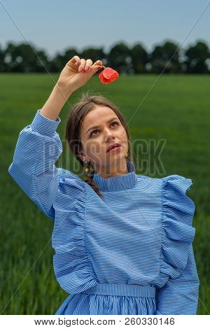 Young Woman In Blue And White Striped Dress Is Holding A Red Poppy Flower Above Her Hed And Looking 