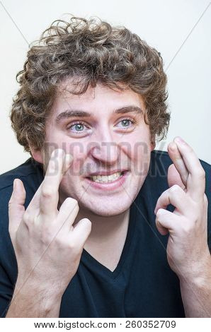 Portrait Of Young Funny Venturesome Curly Man Holding Crossed Fingers In Hope On White Background.