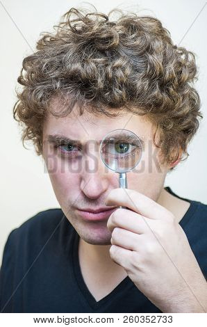 Portrait Of Young Caucasian Ethnicity Questionably Looking On Camera Through Magnifying Lens On Whit