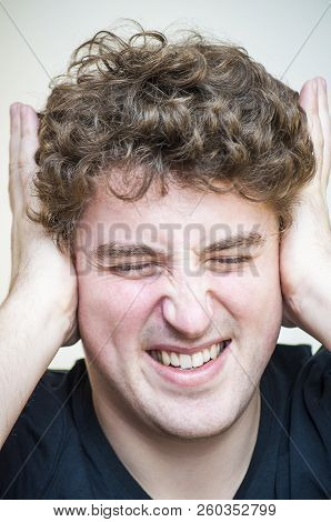 Portrait Of Young Stressed Curly Man Covers His Ears From Noise On White Background.