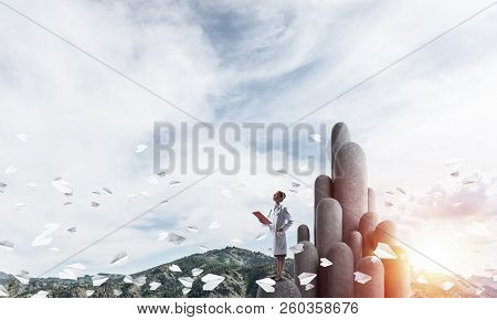 Young Female Doctor With Folder In Hands Satnding On Stone Column