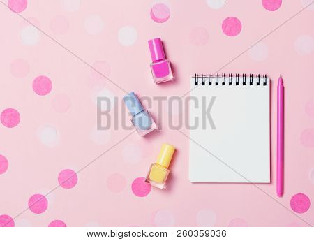 Empty Note Pad And Colorful Nail Polishes On Pink Confetti Background.