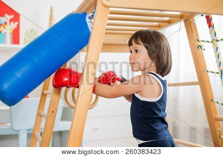 A Small Child Is Engaged In Boxing On A Wooden Home Sports Complex. Girl In Boxing Gloves Hits The P