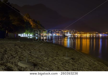 Night View Of The Illuminated Seaside Town Of Baska Voda In Croatia. In The Foreground Is A Pebble B