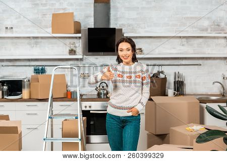 Smiling Young Woman Doing Thumb Up Gesture Near Ladder In Kitchen At New Home