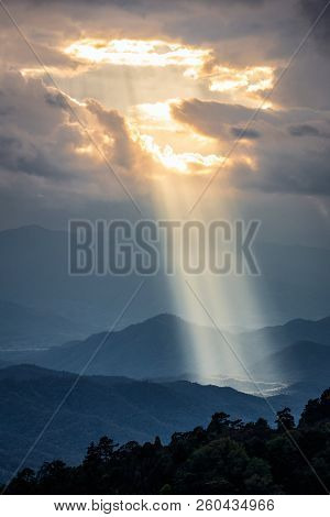 Bright Sunlight Shining Through Hole Of Clouds To Dark Scene Of Mountain Range Before Sunset In Thai