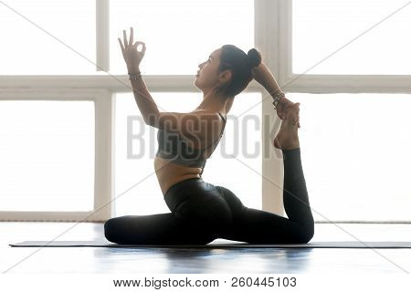 Young Woman Practicing Yoga, Doing One Legged King Pigeon Exerci