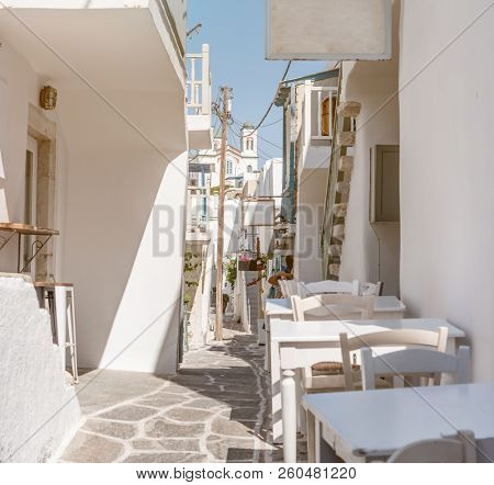 Beautiful narrow street with white houses in Mikonas island, Greece. Traditional narrow street with white facedes of buildings and blue doors