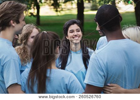 Meeting Of Young Volunteers Team In Park. Happy People Embracing In Circle, Copy Space