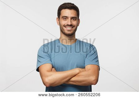 Indoor Portrait Of Young European Caucasian Man Isolated On Gray Background, Standing In Blue T-shir