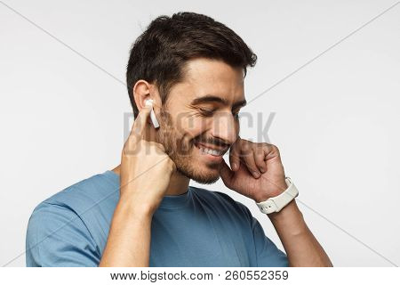 Young Man Wearing Wireless Earbuds And Blue T Shirt, Listening To His Favorite Musical Album Online,