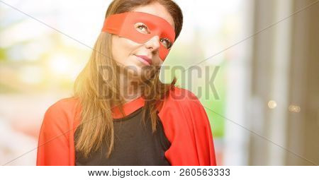 Middle age super hero woman wearing red mask and cape thinking and looking up expressing doubt and wonder