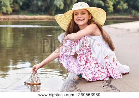 girl playing with a toy sailing ship by the river