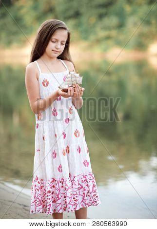 girl playing with a toy sailing ship by the river