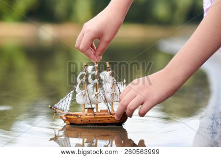 girl playing with a toy sailing ship by the river, hand closeup