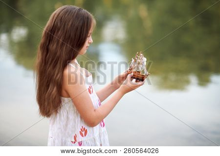 girl playing with a toy sailing ship by the river