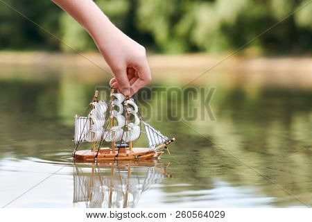 girl playing with a toy sailing ship by the river, hand closeup