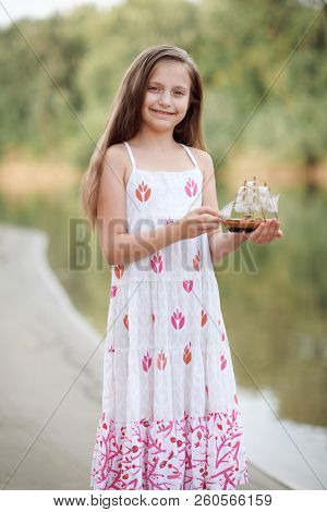 girl playing with a toy sailing ship by the river