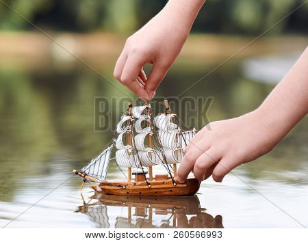 girl playing with a toy sailing ship by the river, hand closeup