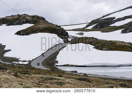 Norwegian scenic route Aurlandsfjellet runs from Aurlandsvangen to Laerdalsoyri. Snow road Bjorgavegen. Two motorcyclists travel to Norway